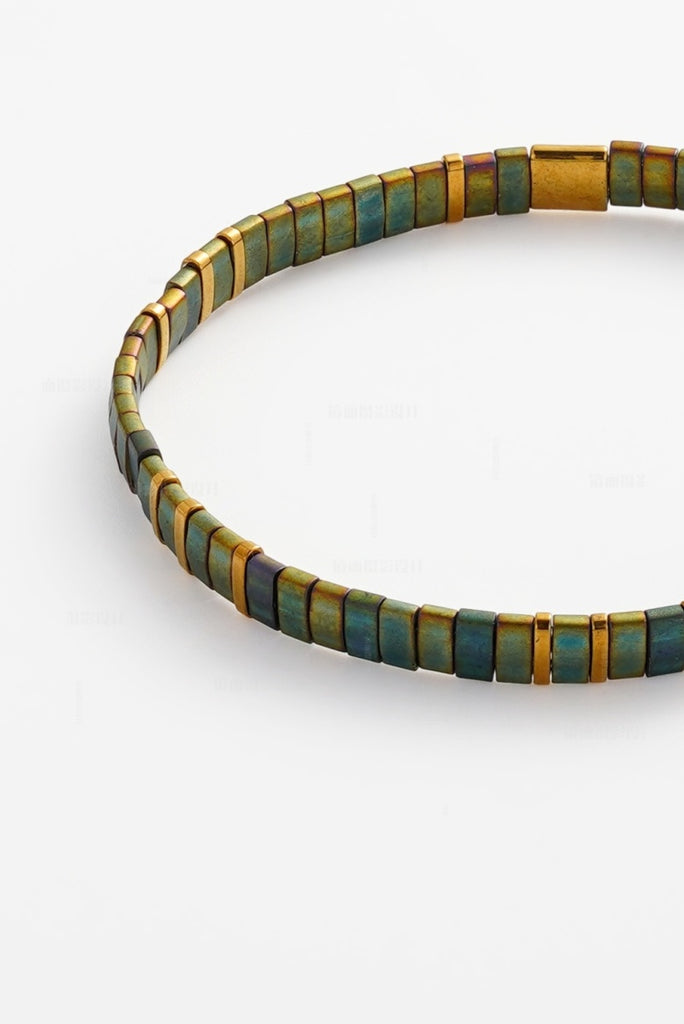 Tile bracelet -olive-Zafino-This minimalist bracelet is crafted from flat, rectangular beads in a deep iridescent olive. The dark, shimmering tones are balanced by slender gold-tone vertical spacers for a refined and modern finish. *18K Gold Plated Solid Stainless Steel Base *17cm Elastic *Water proof: Can be worn in the ocean or pool-Pash + Evolve
