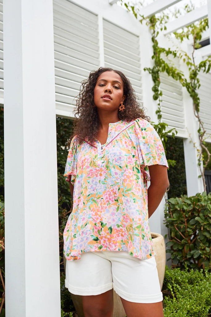 Botanical Blouse - Sunset Hydrangea-Isle of Mine-The Botanical Blouse offers a sophisticated addition to your wardrobe, effortlessly elevating your style. The V-neck with half-button detailing, short flutter sleeves, and delicate ladder lace detail add a touch of effortless femininity. Pair it with a maxi skirt and simple accessories for a polished office ensemble. FEATURES: V-neck with half-button detail Flutter sleeves Ladder lace detail Relaxed hem Plain Material: 100% Viscose Print Material: 100% Rayon 
