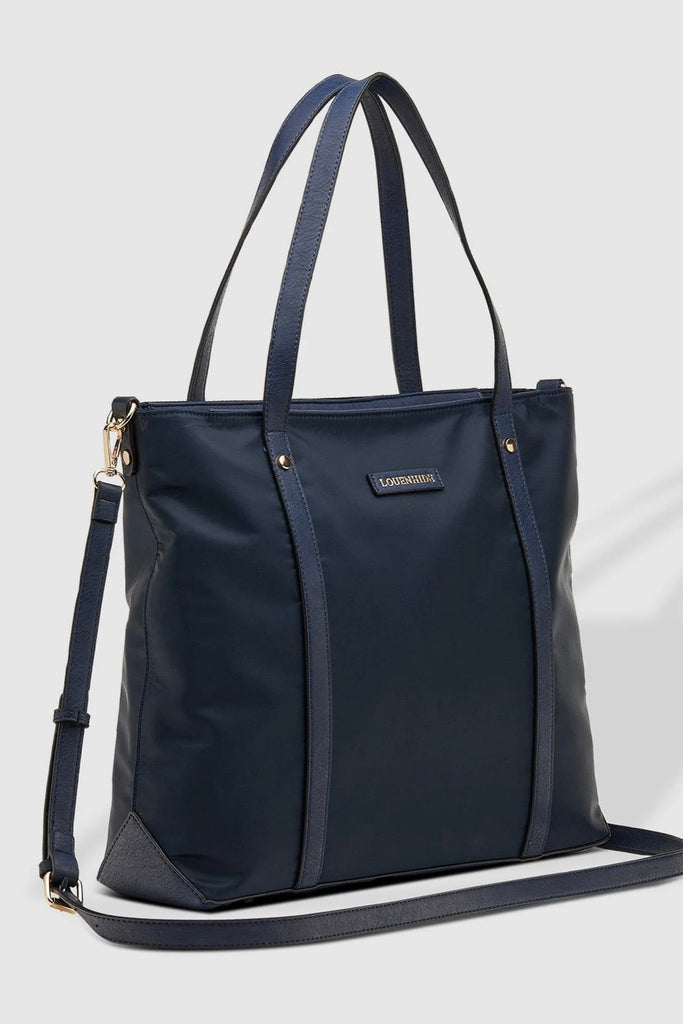 Nora Nylon Tote Bag - Navy-Louenhide-The Louenhide Nora Navy Nylon Tote Bag is the perfect combination of practicality and style. With its spacious interior, this tote bag is perfect for carrying your daily essentials. It features one zip pocket and two slip pockets in the main compartment, as well as a backside zip pocket and feet on the base to keep your belongings safe and secure. The backside suitcase sleeve allows you to easily attach the tote to your luggage for added convenience. The adjustable and d