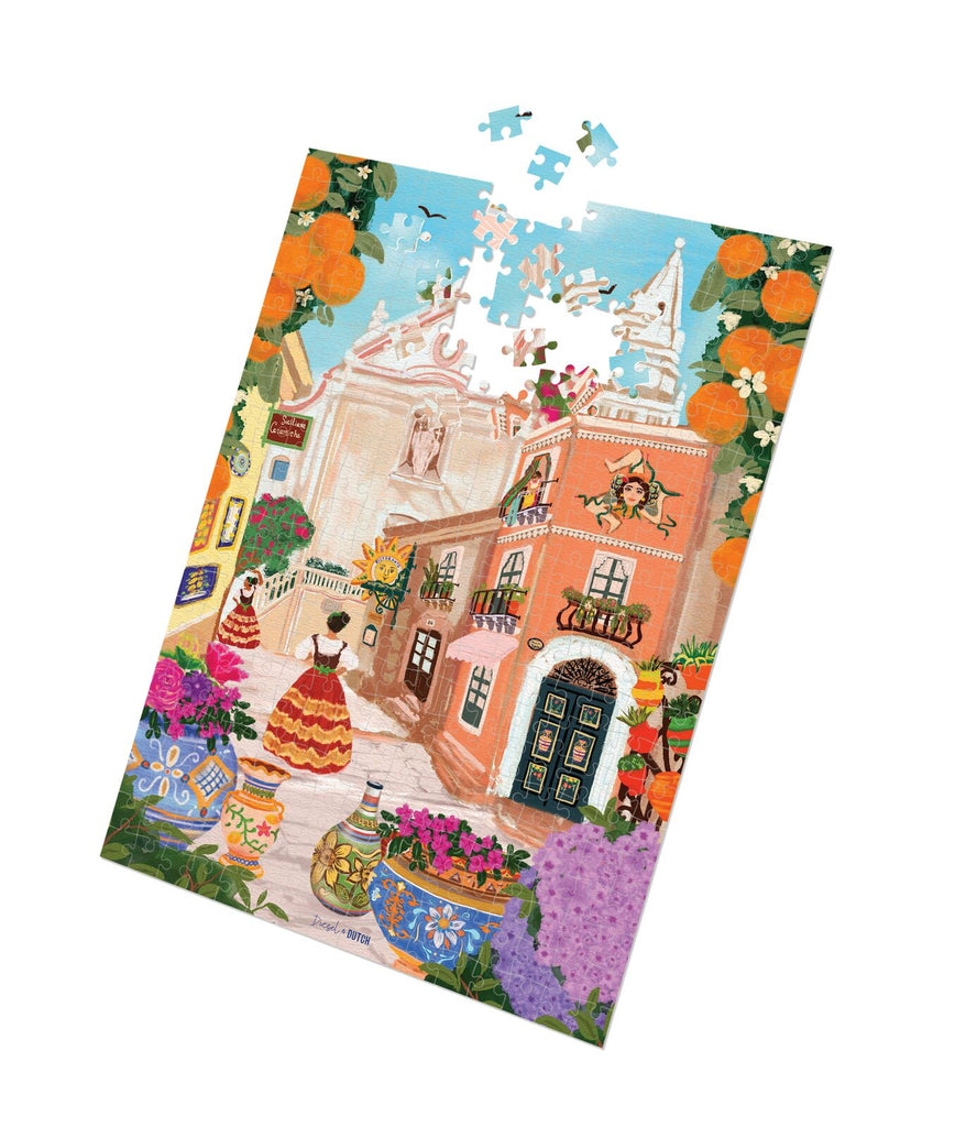 Sicilian Dreamscape - 1000pc-Diesel & Dutch-Transport yourself to the sun-kissed streets of Taormina with this vibrant art print! Let the essence of Sicily fill your space as you admire the iconic Trinacria symbol and breathe in the sweet scent of orange trees. This illustration captures the charm of Taormina's landmarks - the stunning Church of St. Joseph and the quaint clock tower. Adorned with colouful ceramic pots and the lively scenes of locals going about their day, its a true celebration of Sicilian 